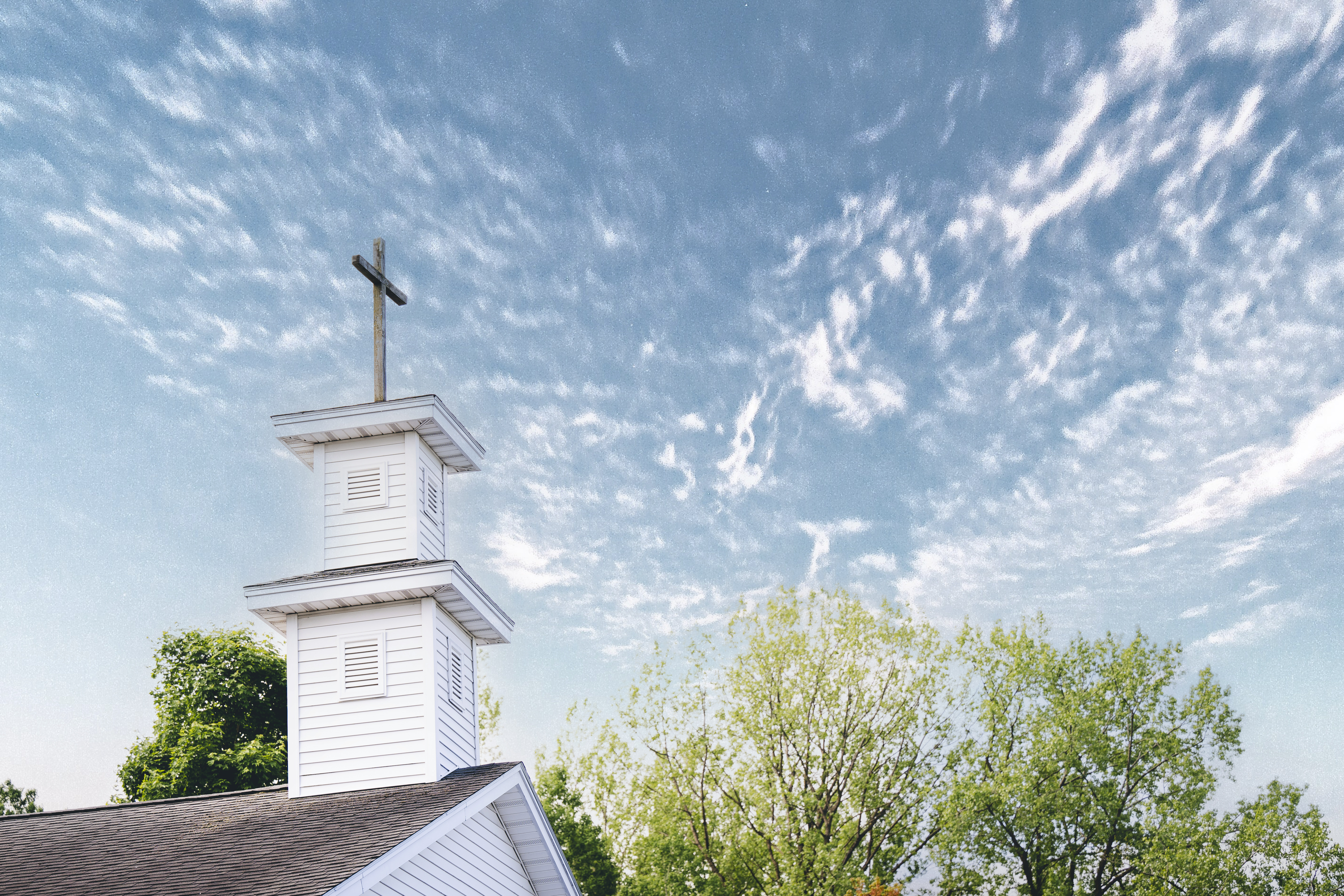 Church with steeple and cross in the foreground on a clear day.